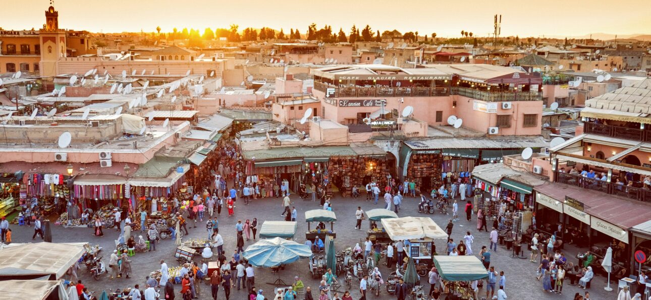The bustling atmosphere of Jemaa el-Fnaa square in Marrakech at sunset, with locals and tourists mingling amid market stalls under a golden sky